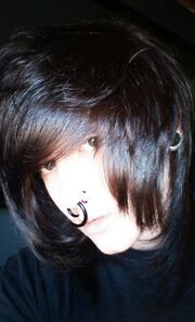 Head and upper body shot of Drakie in real life. He has brown hair, and has one hand on his head.